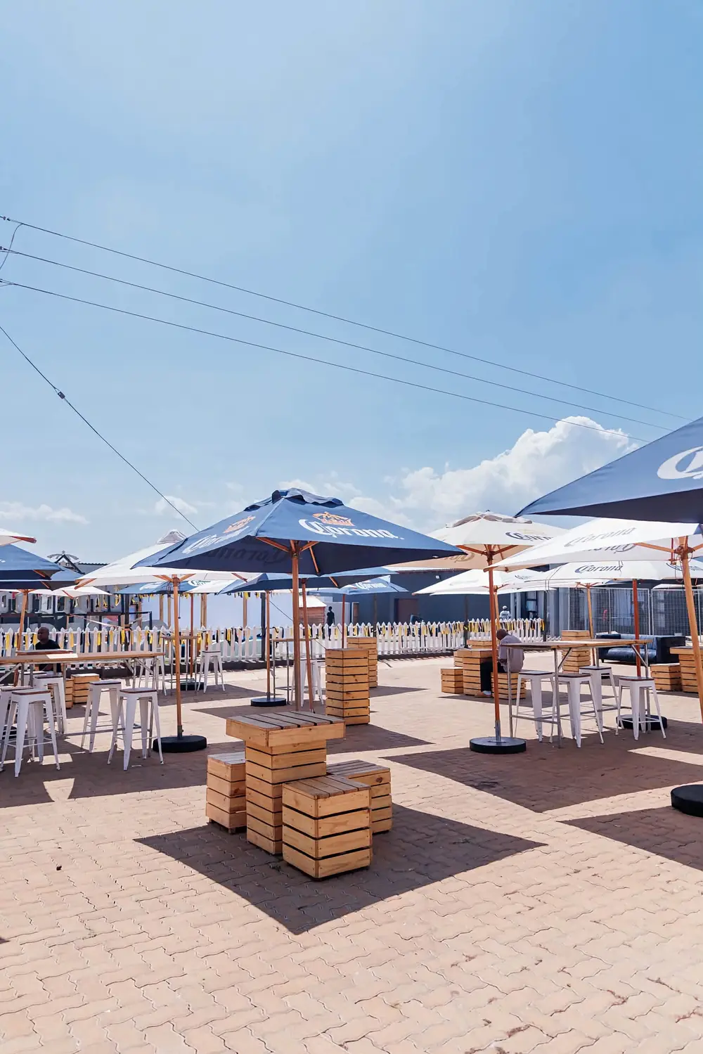 Paved beer garden with Corona umbrellas, crate tables and high stools