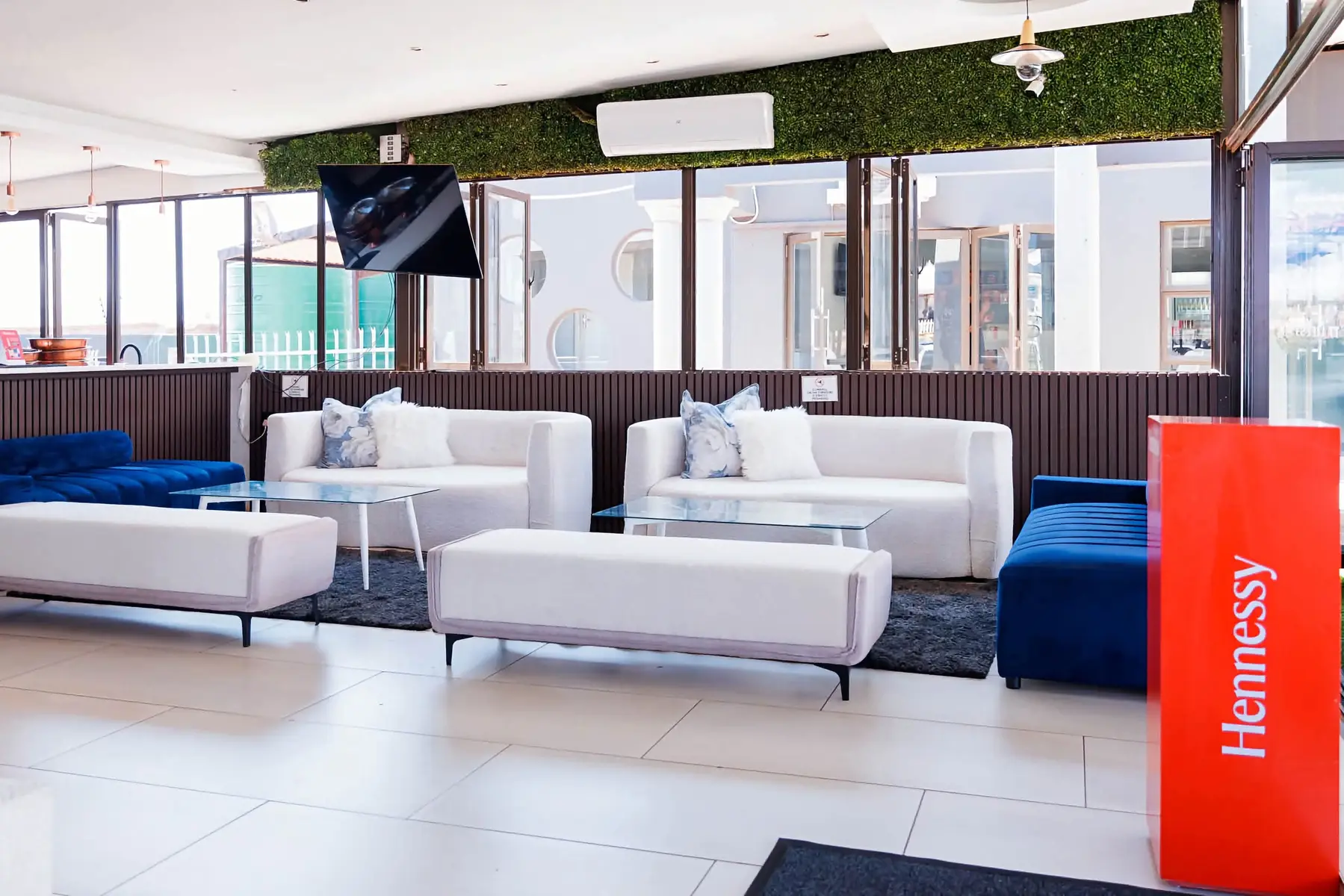 Indoor lounge with white couches, blue velvet seating and a Hennessy display