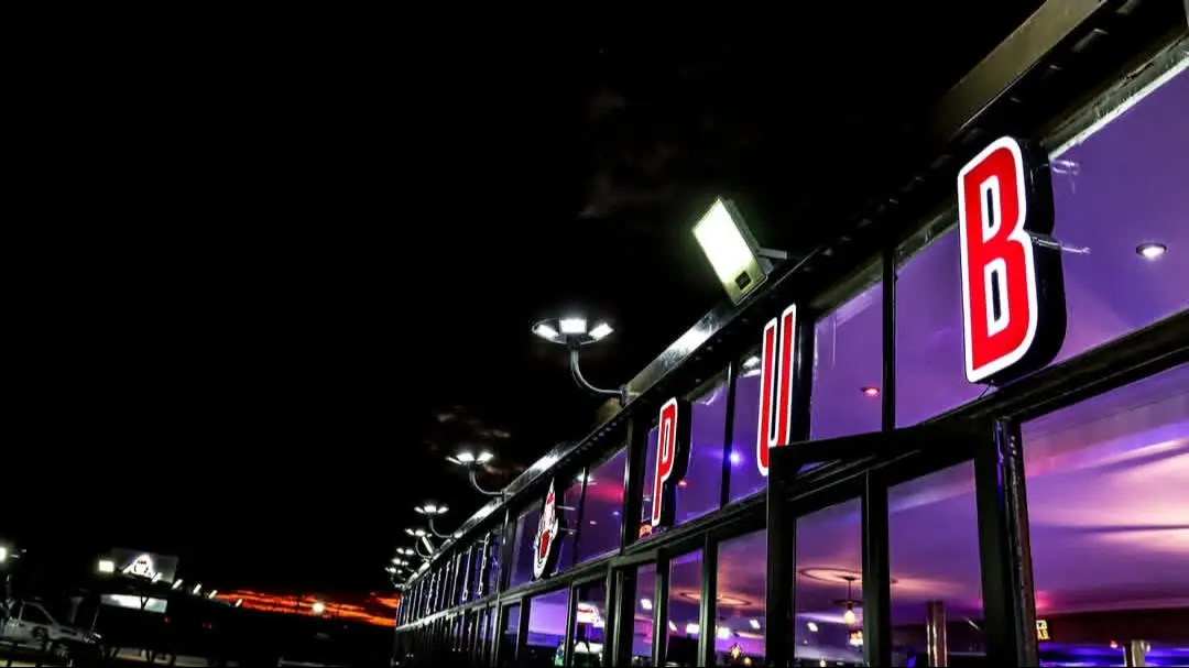 The pub at night, glowing purple through the windows with lit red PUB letters