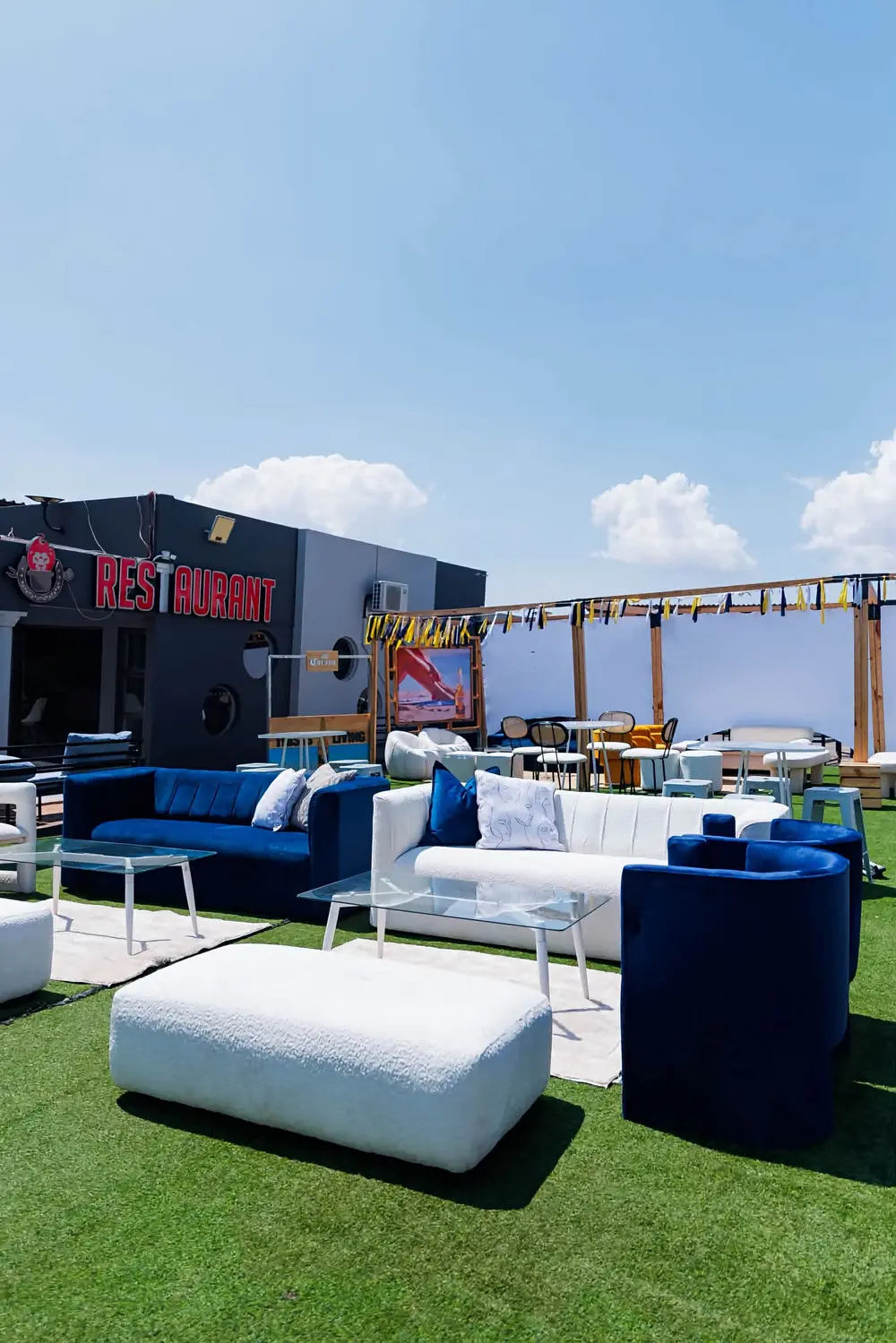 Outdoor lounge on artificial grass with blue and white couches beside the restaurant sign