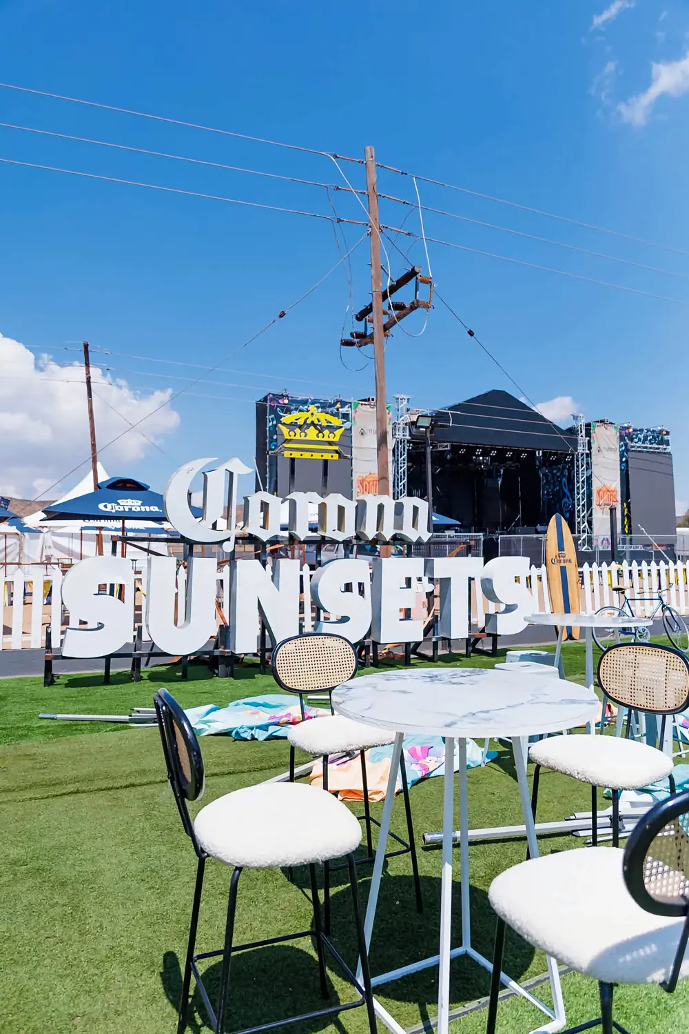 Corona Sunsets lettering in front of the main festival stage, with cocktail tables on the grass